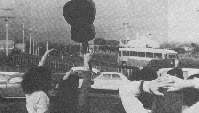 Black and white photo showing people waving farewell to bus.