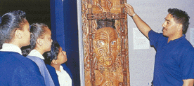 Three children look at a carving, with an adult pointing to it.