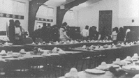 Black and white photo showing people preparing dining room.