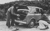 Black and white photo showing two people at car boot.