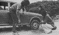 Black and white photo of two people with car.