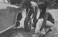 Black and white photo of two people changing car tyre.