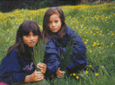 Two children sitting on grass holding cabbage tree leaves.